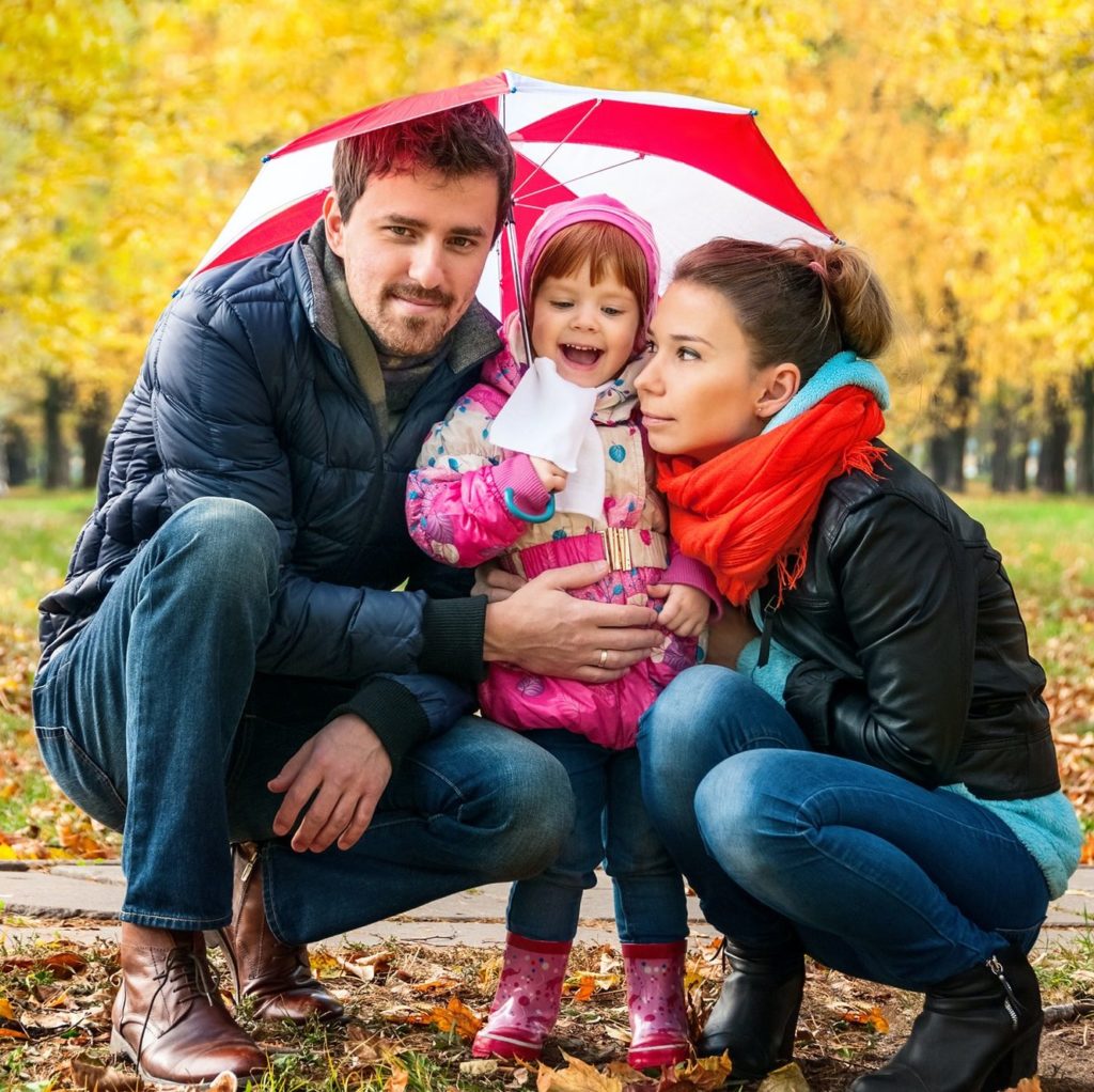 Happy young family under an umbrella in an autumn park